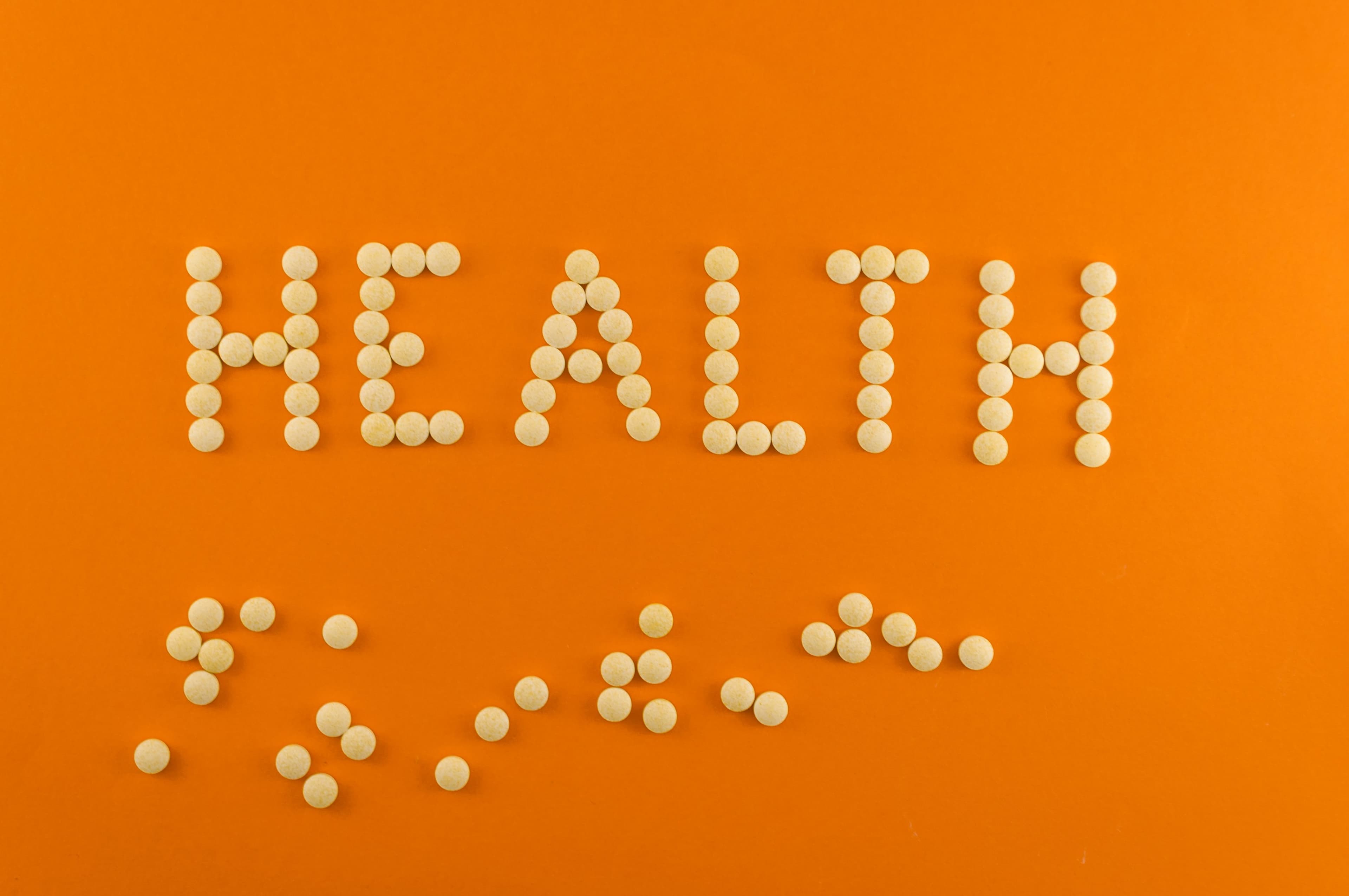 The word 'Health' spelled out using white supplement pills on an orange background, symbolizing wellness and the role of supplements like NAC