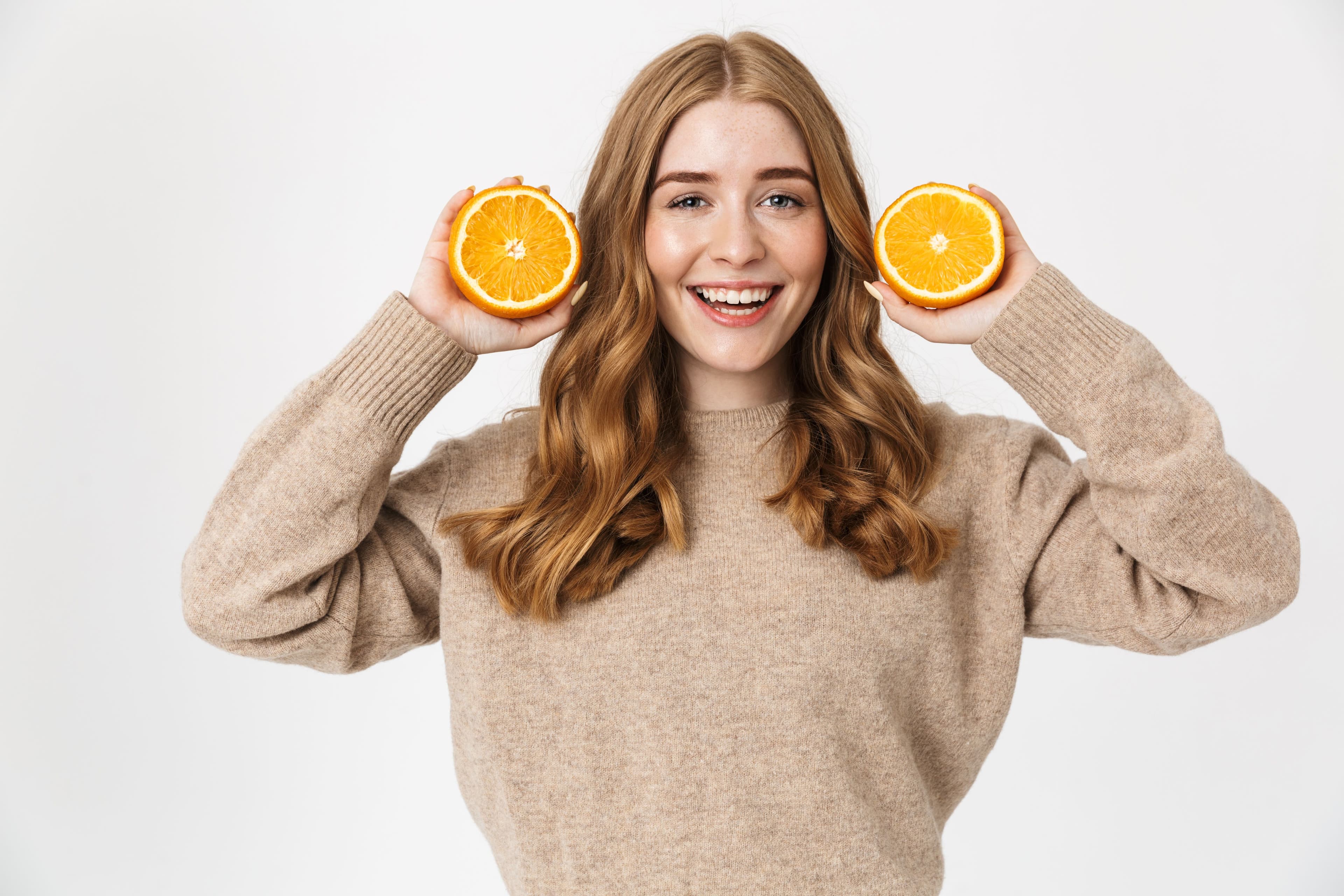 Smiling young woman holding sliced oranges, symbolizing Vitamin C benefits for immunity, radiant skin, and overall wellness.