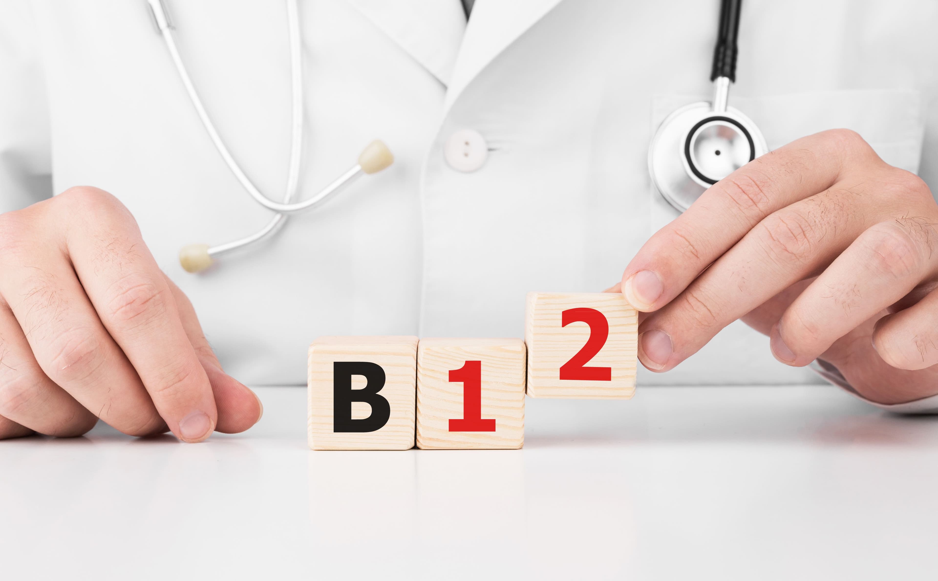 A doctor holding wooden cubes spelling 'B12' with a stethoscope in the background, symbolizing the importance of Vitamin B12 for health and wellness