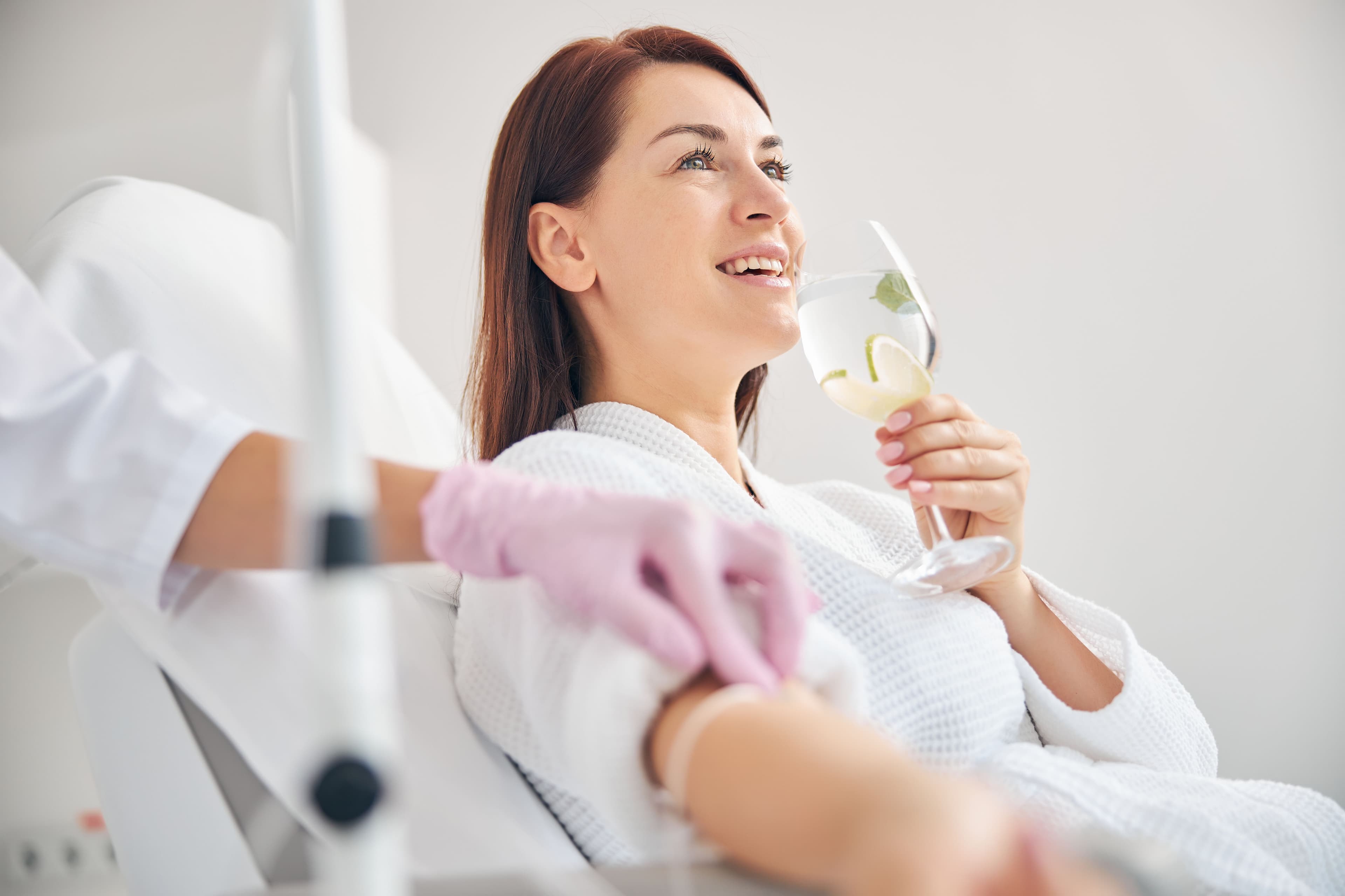 A smiling woman enjoying a refreshing beverage while receiving IV hydration therapy at a wellness spa, highlighting the benefits of hydration and energy recovery in Charlotte, NC.